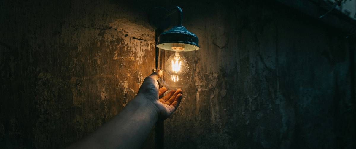 how to replace wall sconce lighting: close-up of hands disconnecting wiring from an old wall-mounted fixture during replacement process